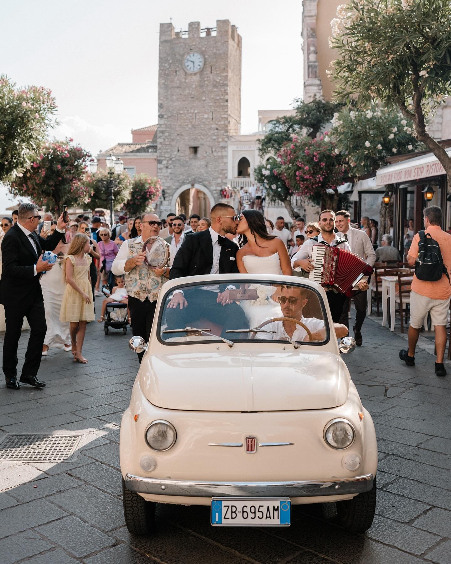 Couple in a vintage car celebrating their wedding in a historic European town square